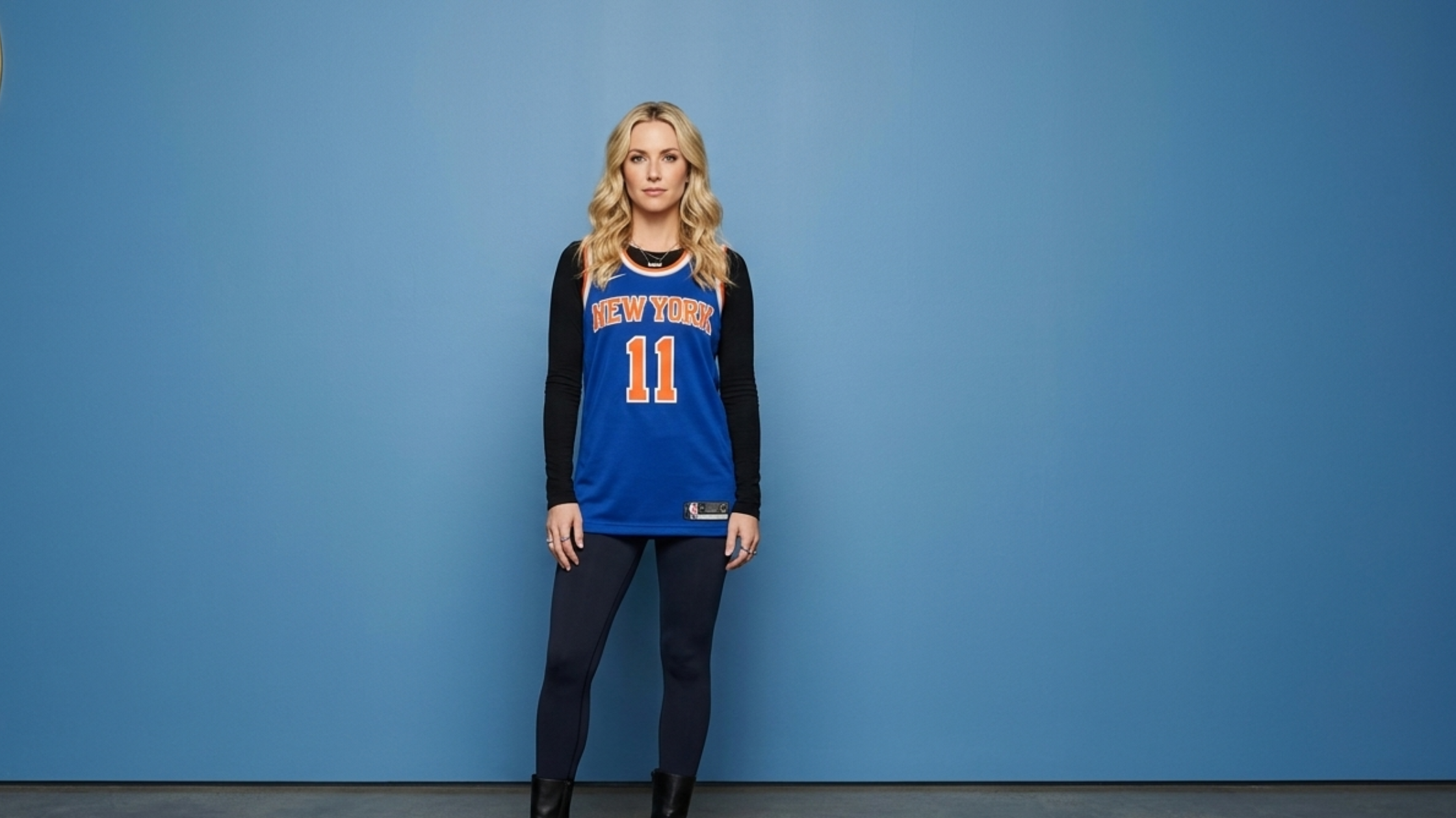 Kim Gordon wearing an oversized New York Knicks inspired blue jersey with orange and white “NEW YORK” graphic during The Tonight Show Starring Jimmy Fallon